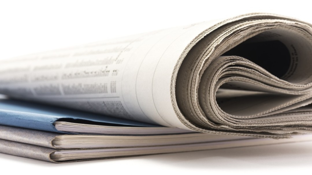 A folded newspaper is lying on a pile of brochures