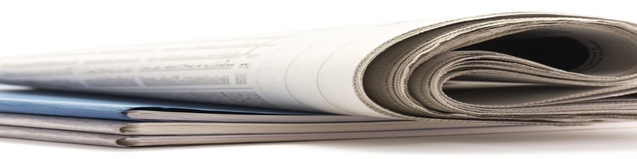 Eine zusammengerollte Zeitung liegt auf einem Broschürenstapel
