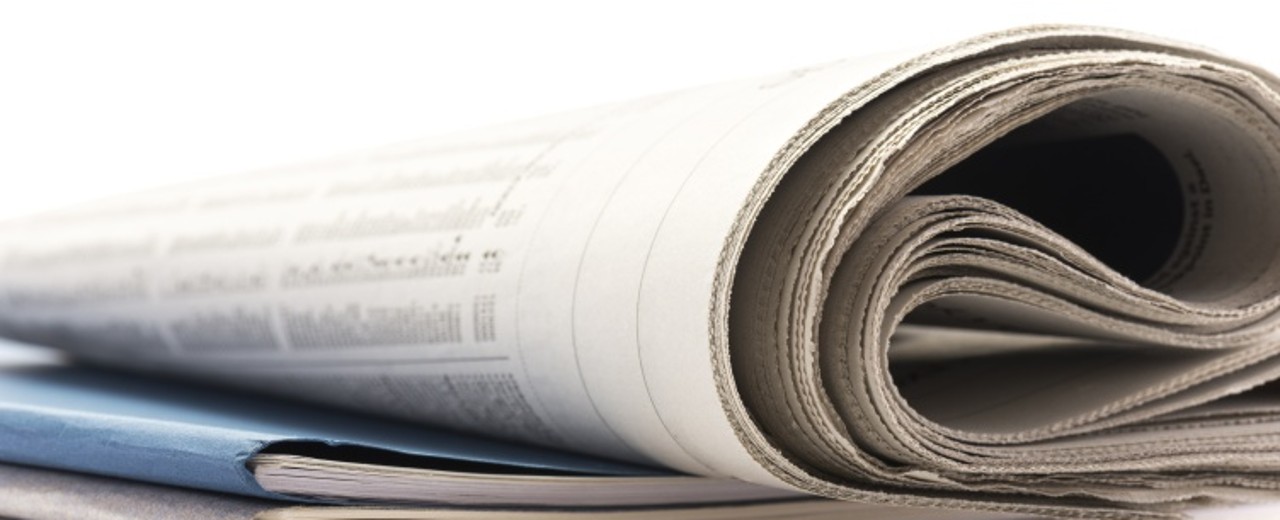 Eine zusammengerollte Zeitung liegt auf einem Broschürenstapel