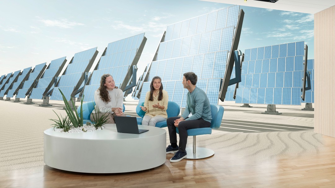 Drei Personen im Gespräch auf Sitzmöbeln neben einem Laptop vor einer großflächigen Darstellung zahlreicher Solarmodule.