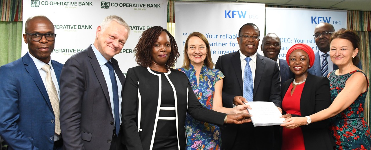 Contract signing betwwen DEG and the Co-opverative Bank Kenya: Group of people presenting official documents in front of partner banners, symbolizing long-term development cooperation.