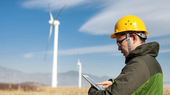 Ein Mann mit einem Tablet-PC steht vor mehreren Windrädern.