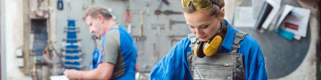 Werkstatt mit zwei Personen bei der Metallbearbeitung, umgeben von Werkzeugen und Maschinen.